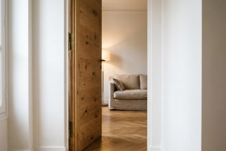 Porte battante en chêne massif entrouverte dans un couloir d'appartement parisien contemporain avec parquet en point de Hongrie