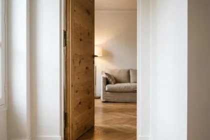 Porte battante en chêne massif entrouverte dans un couloir d'appartement parisien contemporain avec parquet en point de Hongrie